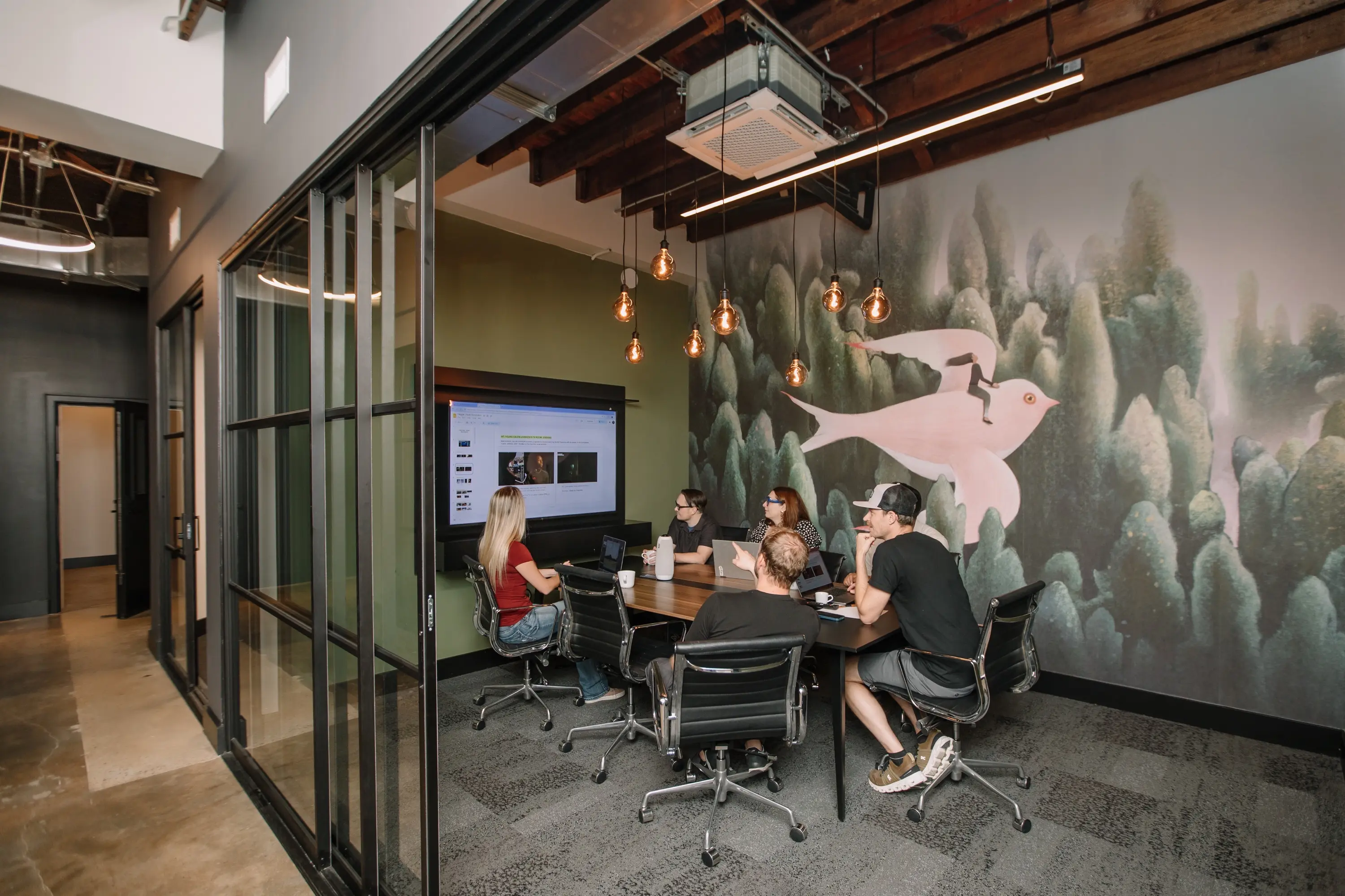 A team meeting in the 8-person conference room, in front of a forest mural