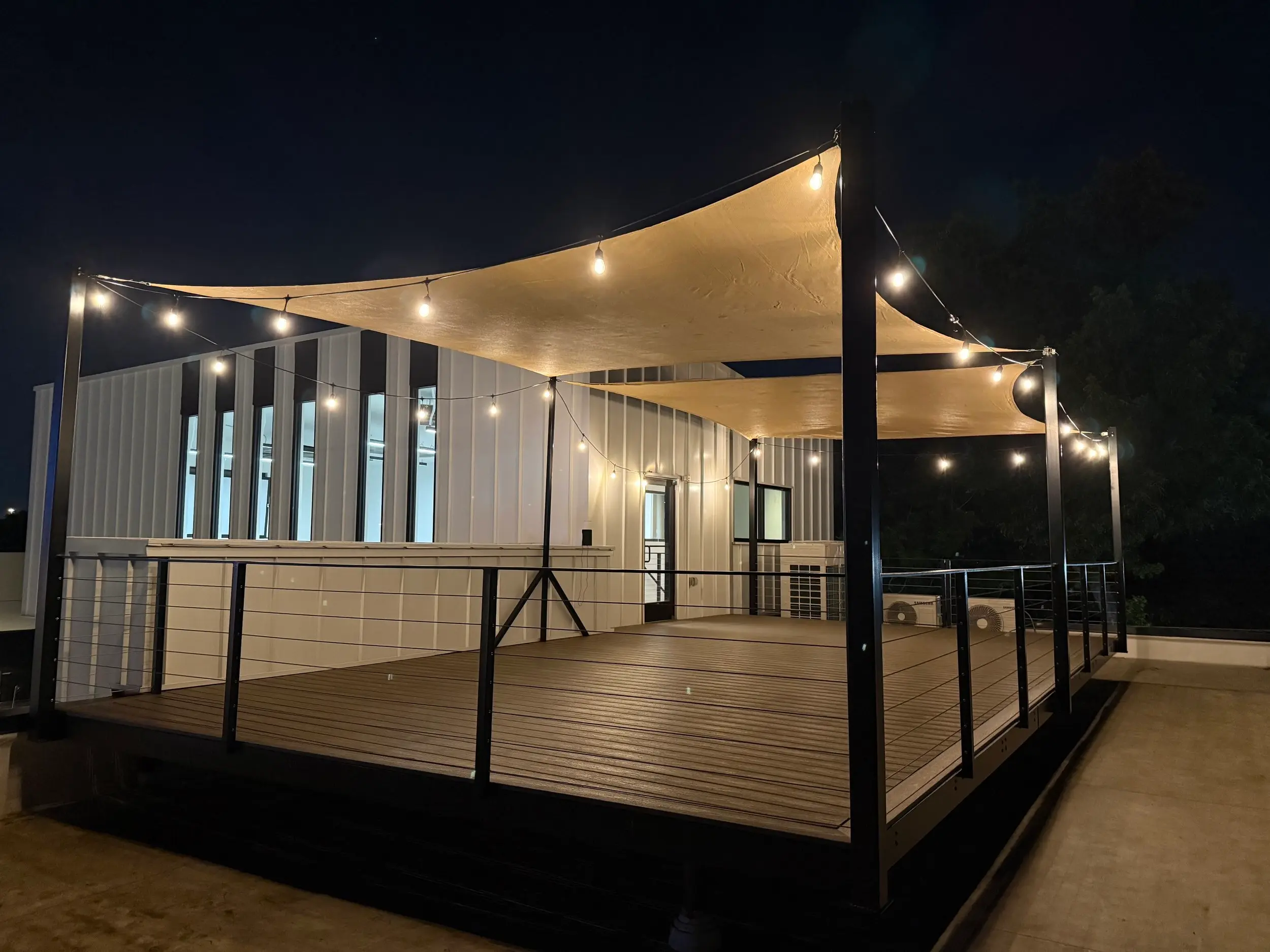 The rooftop deck at night under string lights and shade sails